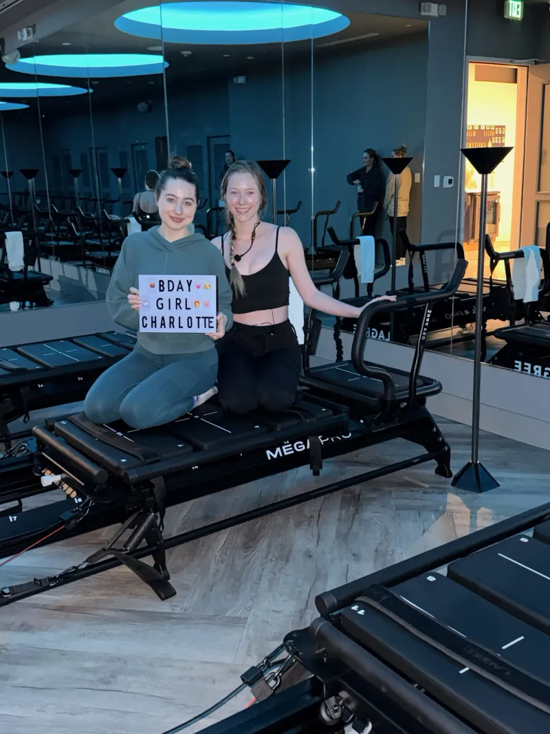 Instructor and birthday member kneel on a Megaformer holding a "Bday Girl" board at TIGHT