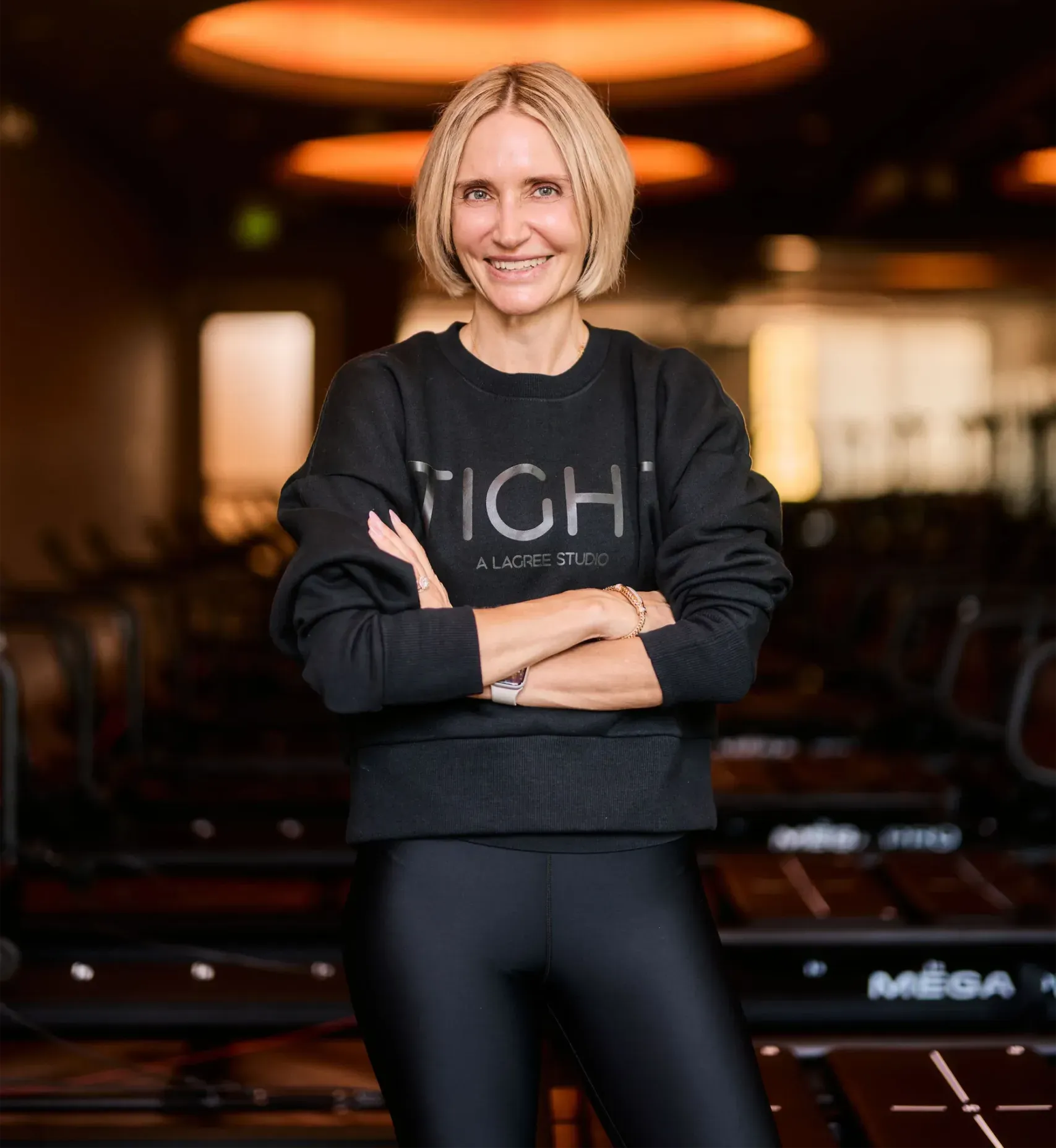 lita-owner-branded-sweatshirt-megaformer-floor-tight-dallas. Lita, owner of TIGHT Dallas, in a branded TIGHT sweatshirt on the Megaformer studio floor
